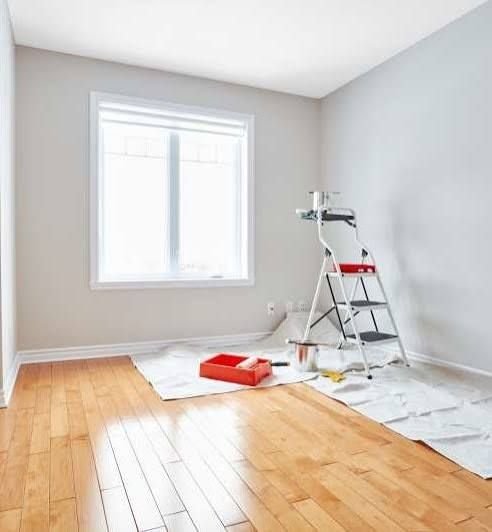 Empty room being painted with drop cloths and a step ladder