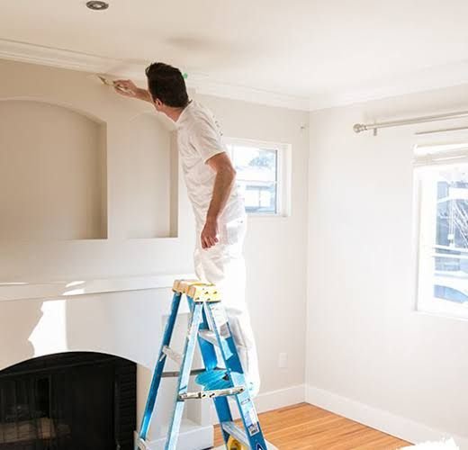 Painter on a ladder brushing trim along the ceiling